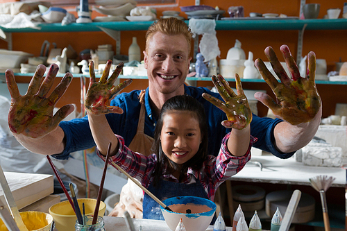 Male potter and girl showing their painted hands in pottery workshop