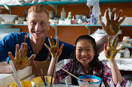 Male potter and girl showing their painted hands in pottery workshop