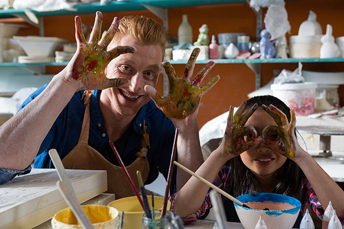 Male potter and girl showing their painted hands in pottery workshop
