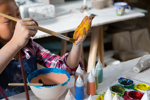 Girl painting her hand with paint brush in pottery workshop