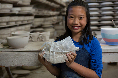 Portrait of happy girl holding clay in pottery workshop