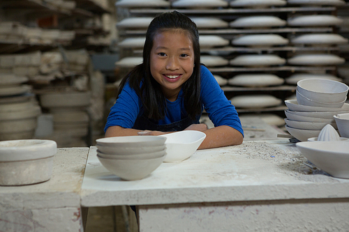 Portrait of happy girl sitting at worktop in pottery workshop