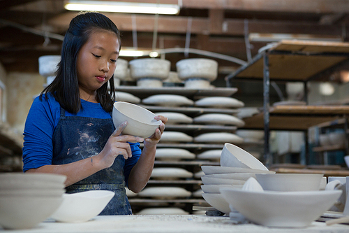 Attentive girl checking bowl at worktop in pottery workshop