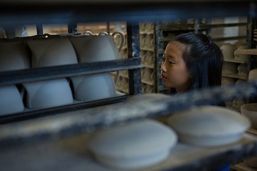 Girl arranging cups in shelf at pottery workshop