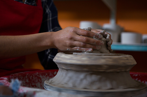 Mid section of female potter molding a clay in pottery workshop