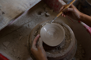 Overhead of female potter molding a bowl with hand tool