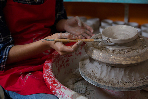 Mid section of female potter molding a bowl with hand tool