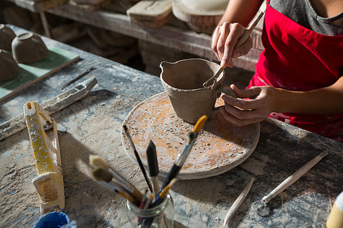 Mid section of female potter carving mug