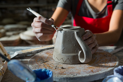 Mid section of female potter carving mug