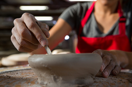 Mid section of female potter molding a bowl with hand tool