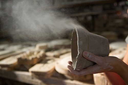 Female potter blowing dust from mud in pottery workshop