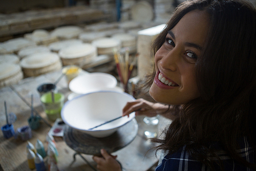 Portrait of female potter painting bowl in pottery workshop