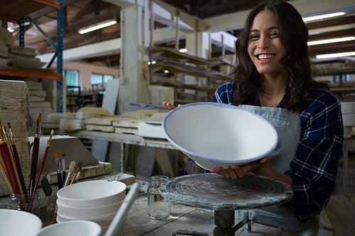 Portrait of female potter painting bowl in pottery workshop