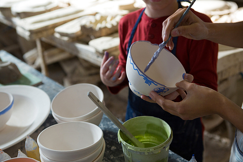 Mid section of female potter and boy painting bowl in pottery workshop