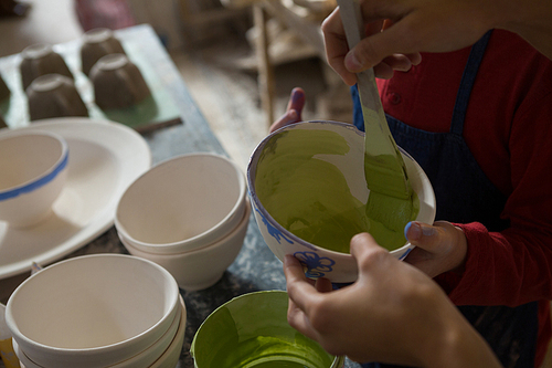 Mid section of female potter and boy painting bowl in pottery workshop