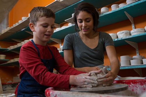 Female potter assisting boy in molding a clay at workshop
