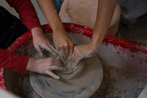 Mid section of female potter assisting boy in molding a clay