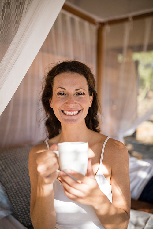 Portrait of happy woman having coffee in canopy bed during morning