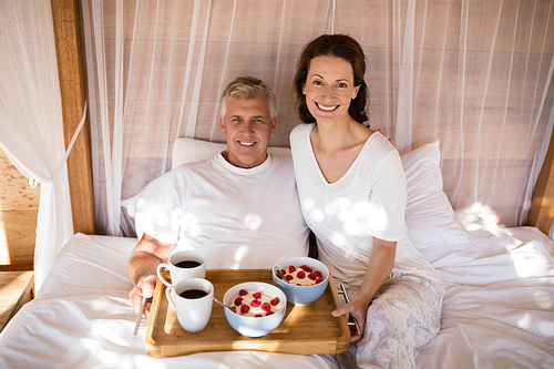 Happy couple having breakfast in canopy bed during morning