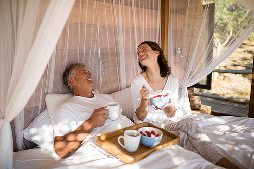 Happy couple having breakfast in canopy bed during morning