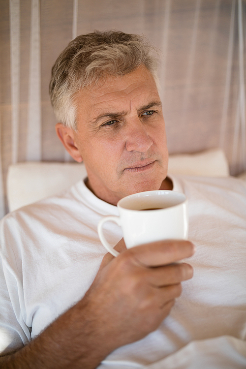 Thoughtful man having coffee on bed during morning