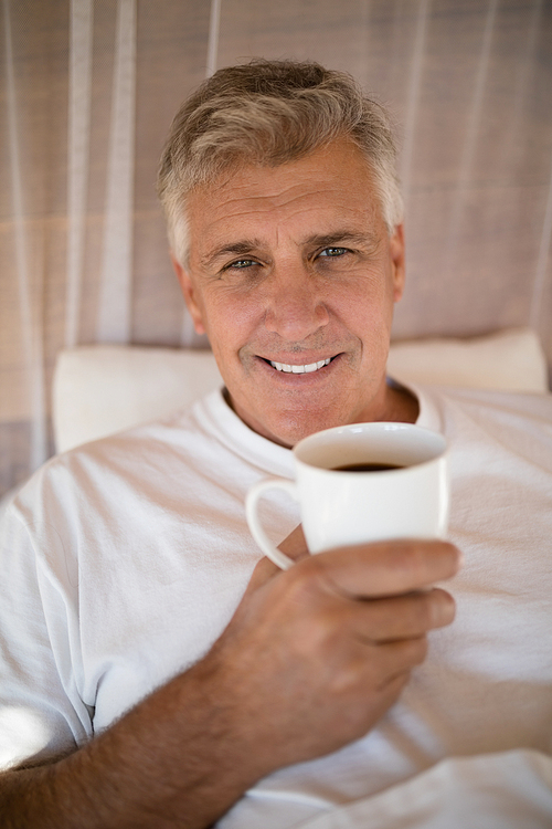 Portrait of happy man having coffee on bed during morning