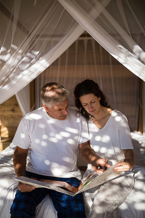 Couple looking at map while relaxing on canopy bed during morning