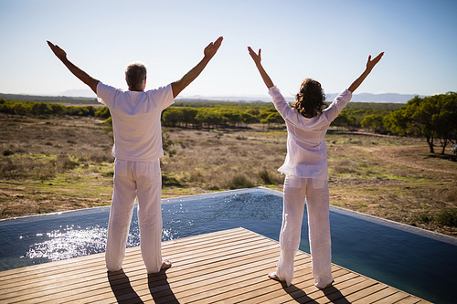 Rear view of couple standing with arms outstretched near poolside on a sunny day