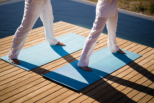 Low section of couple practicing yoga on at poolside on a sunny day