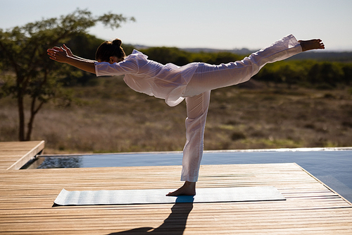 Woman practicing yoga on at poolside on a sunny day