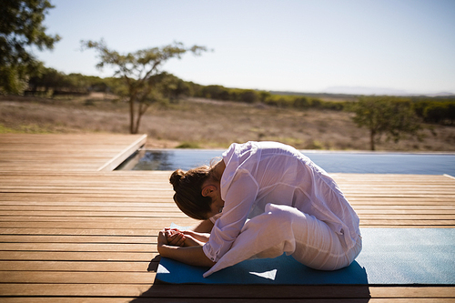 Woman practicing yoga on at poolside on a sunny day