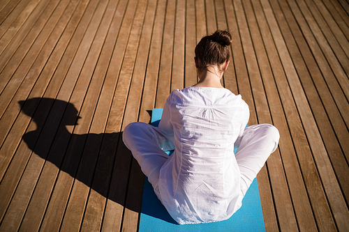 Rear view of woman practicing yoga on wooden plank on a sunny day