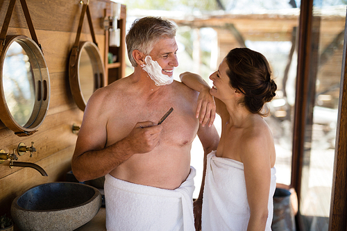 Smiling couple interacting while shaving in cottage during safari vacation