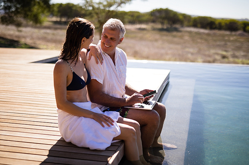 Couple interacting while using laptop near poolside during safari vacation