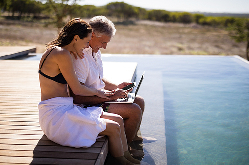 Couple using laptop near poolside during safari vacation