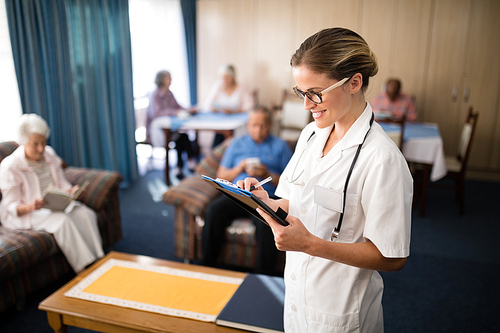 Smiling female doctor writing in file against senior people sitting at nursing home