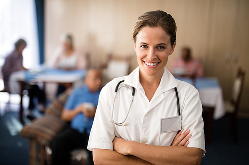 Portrait of smiling female doctor standing with arms crossed at retirement home