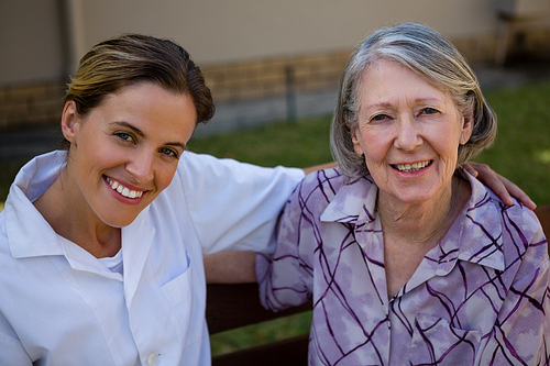 Portrait of happy senior woman and doctor sitting on bench in yard