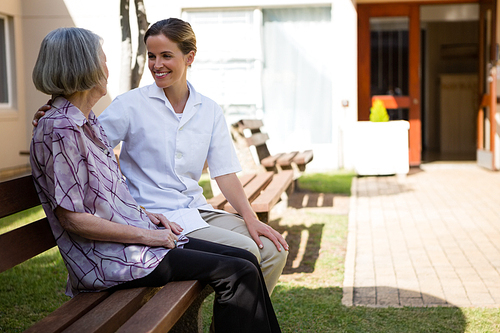 Senior woman talking to doctor while sitting on bench in yard