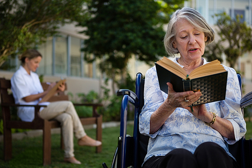 Senior woman reading book while doctor sitting in background at park