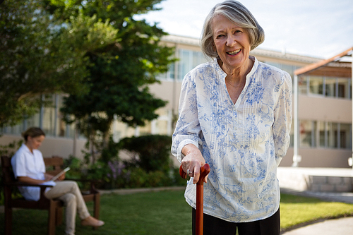 Portrait of smiling senior woman with doctor in background at park