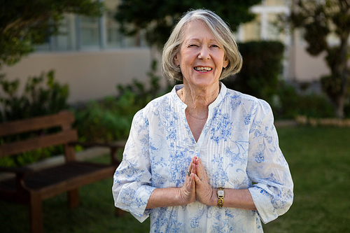 Portrait of happy senior woman standing in prayer position at park