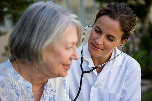 Female doctor examining senior woman with stethoscope in park