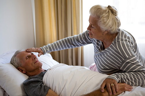 Senior woman sitting by husband sleeping on bed in nursing home