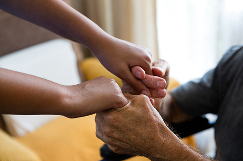 Cropped image of female doctor and senior man holding hands in nursing home