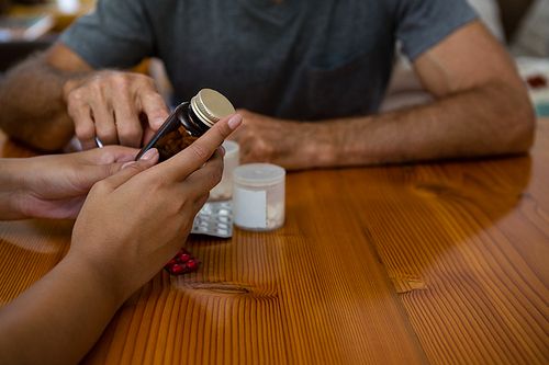 Midsection of doctor guiding senior man in taking medicine at table