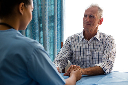 Female doctor holding hands of senior man while consoling at nursing home