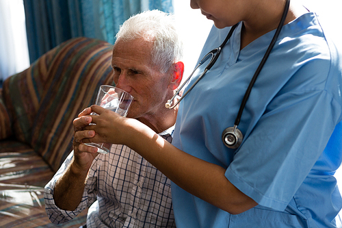 Midsection of female doctor assisting senior man in drinking water at nursing home