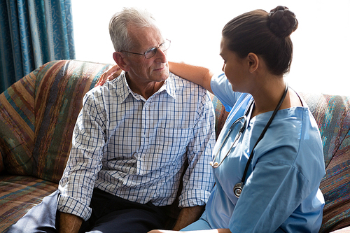 Side view of female doctor consoling senior man while sitting on sofa