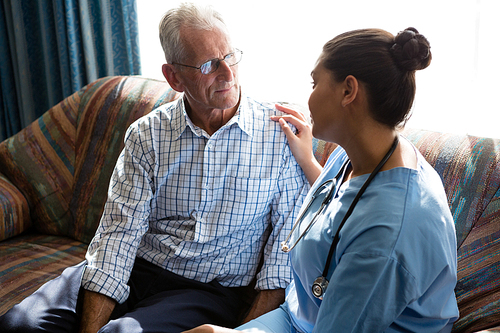 Side view of female doctor consoling senior man on sofa in nursing home